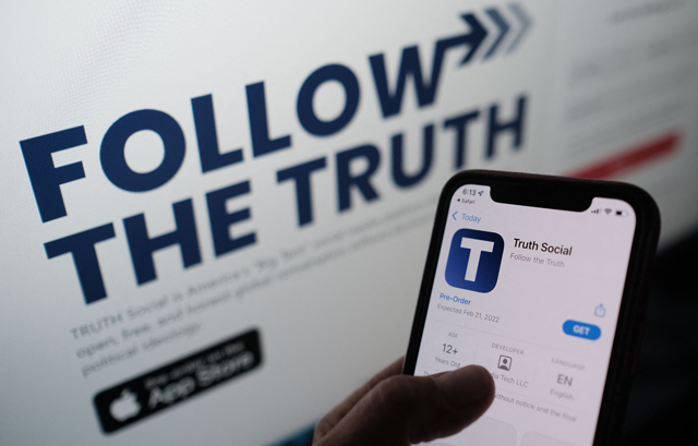 In this file photo illustration taken on October 20, 2021, a person is checking the app store on a smartphone for 'Truth Social', with its website on a computer screen in the background, in Los Angeles (AFP photo)