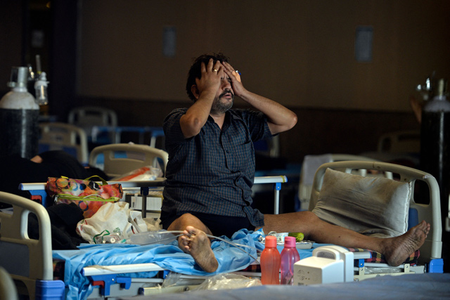 A COVID-19 coronavirus patient reacts while sitting on a bed inside a banquet hall temporarily converted into a COVID care centre in New Delhi on Monday  (AFP photo)