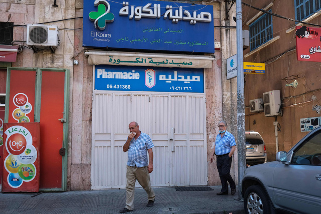 Men walk in front of the shuttred door of a pharmacy in the northern Lebanese city of Tripoli, during a nationwide strike of pharmacies to protest against a severe shortage of medicine, on Friday (AFP photo)