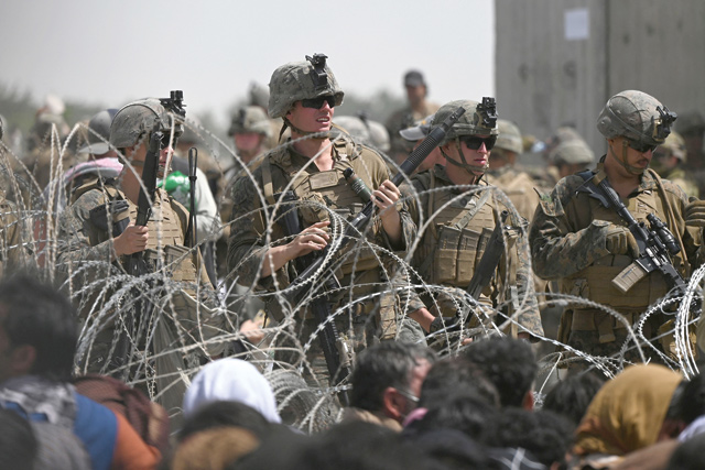 US soldiers stand guard behind barbed wire as Afghans sit on a roadside near the military part of the airport in Kabul on Friday, hoping to flee from the country after the Taliban's military takeover of Afghanistan (AFP photo)