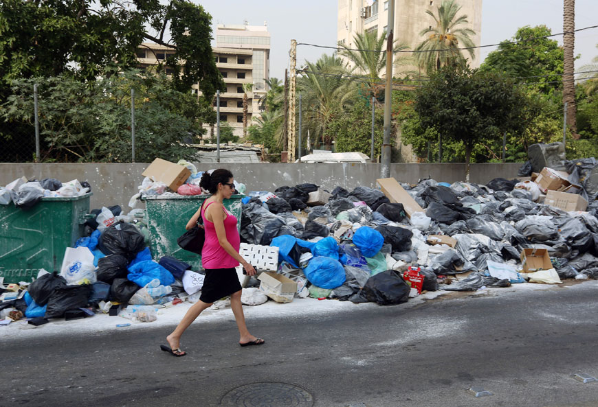 A Lebanese woman walks past a pile of garbage covered with white pesticide in Antelias, north of Beirut, Lebanon, on Monday (AP photo)
