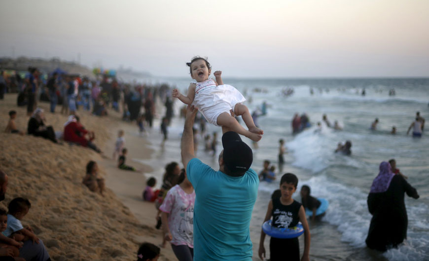 A Palestinian man lifts his daughter as he enjoys the warm weather with his family on a beach along the Mediterranean Sea in the northern Gaza Strip on Friday  (Reuters photo)