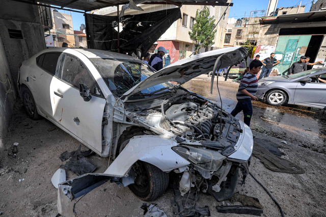 People stand near a vehicle destroyed during an Israeli military operation at the Jenin camp for Palestinian refugees in the occupied West Bank on Tuesday (AFP photo)