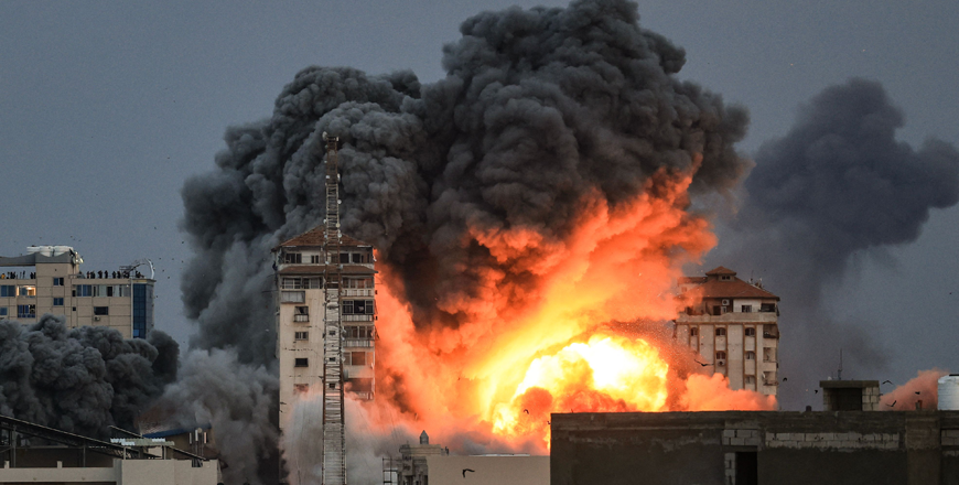 People standing on a rooftop watch as a ball of fire and smoke rises above a building in Gaza City on Sunday during an Israeli air strike (AFP photo)