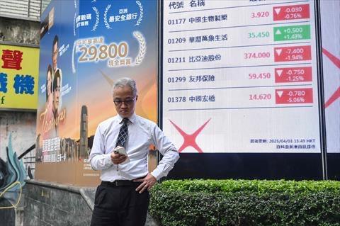 A man checks his phone next to an electronic board showing stocks on the Heng Seng Index in Hong Kong on April 3, 2025 (AFP photo)