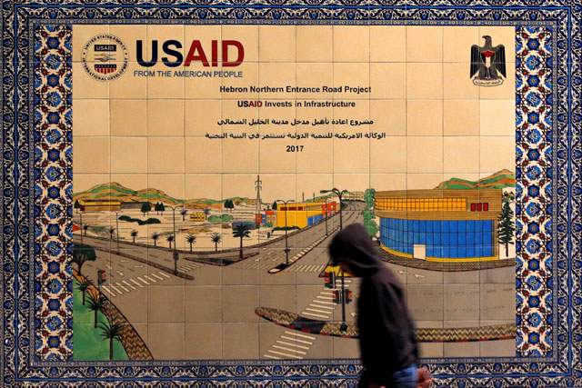 A Palestinian walks past a ceramic sign of a US Agency for International Development project in Hebron in the Israeli-occupied West Bank on Thursday (Reuters photo)