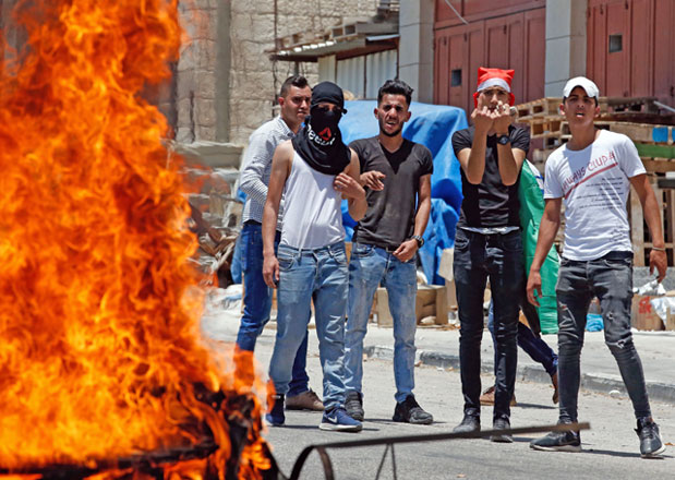 Palestinians carrying stones stand behind a burning tyre during a protest against a US-led meeting this week in Bahrain on the Palestinian-Israeli conflict, in the village of Halhul, near the West Bank city of Hebron, on Monday (AFP photo)
