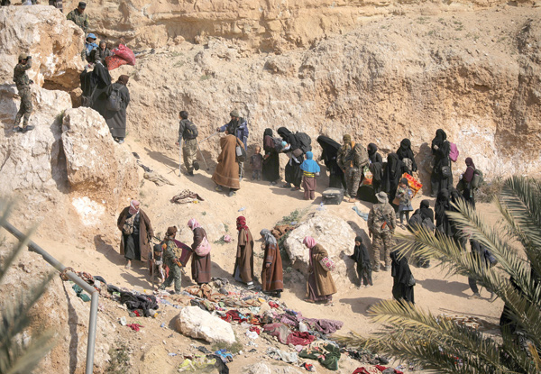 Daesh fighters and their families walk as they surrendered in the village of Baghouz, Deir Ezzor province, Syria, on Tuesday (Reuters photo)