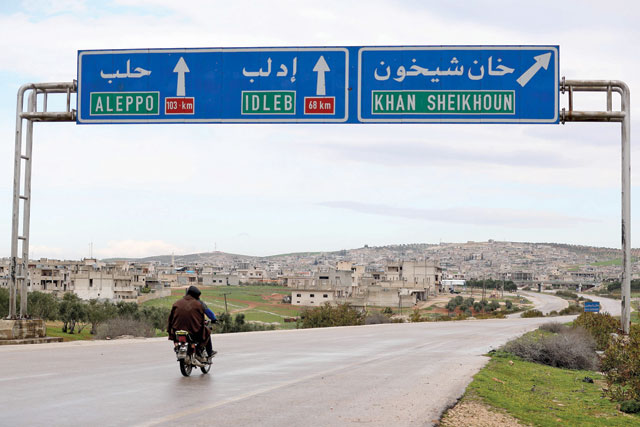 In this file photo taken on February 28, two Syrian men drive past road signs in Khan Sheikhoun (AFP photo)