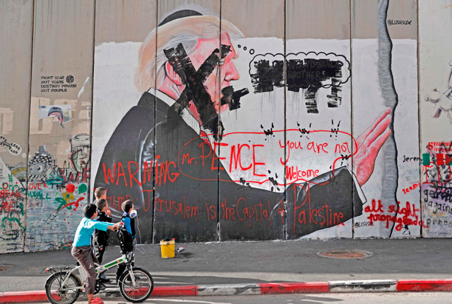 Palestinian children look at vandalised graffiti depicting US President Donald Trump and slogans against US Vice President Mike Pence painted on Israel’s controversial separation barrier in the West Bank city of Bethlehem, during confrontations with Palestinian protesters near an Israeli checkpoint on Thursday (AFP photo)
