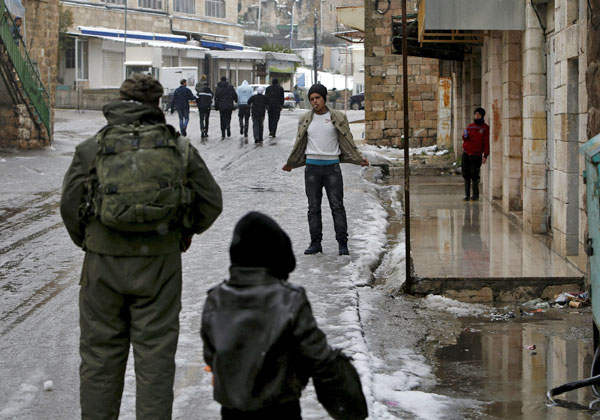 An Israeli soldier inspects a Palestinian during a snowstorm in the West Bank city of Hebron, on Tuesday (Reuters photo)