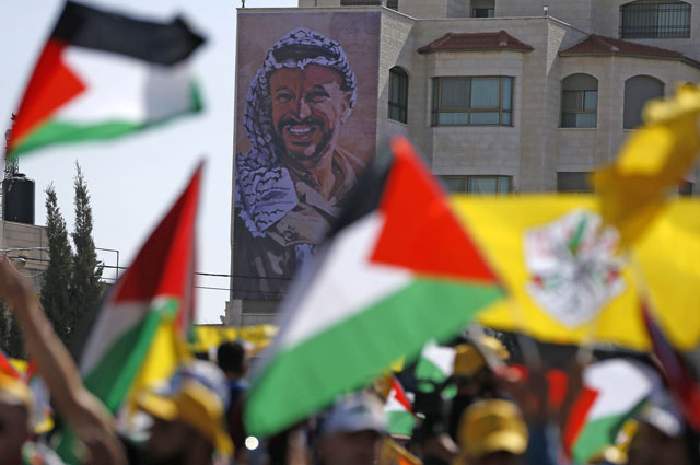Palestinians wave their national flag and the Fateh Party flag as they take part in a rally marking the 12th anniversary of the death of Palestinian leader Yasser Arafat (portrait) in the West Bank city of Ramallah on Friday (AFP photo)