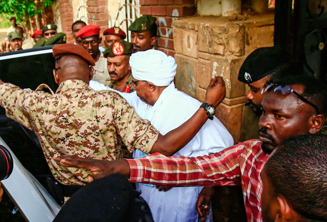   Sudan's ousted president Omar Al Bashir (centre) is escorted into a vehicle as he returns to prison following his appearance before prosecutors over charges of corruption and illegal possession of foreign currency in the capital Khartoum on Sunday (AFP photo)