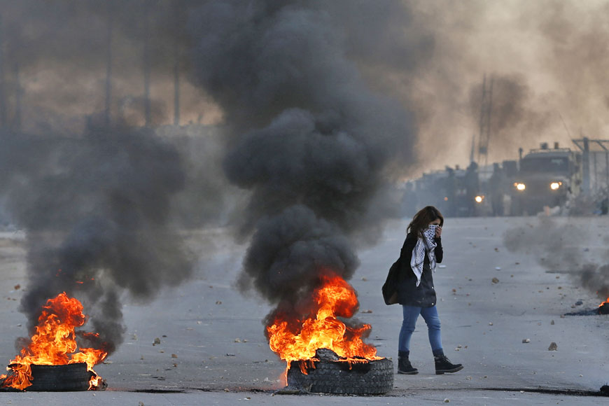 A Palestinian female protester covers her face as she walks past burning tyres during confrontations with Israeli forces near the Ofer Israeli military prison, located near the West Bank town of Betunia, on Friday following a march by young Palestinians (AFP photo)