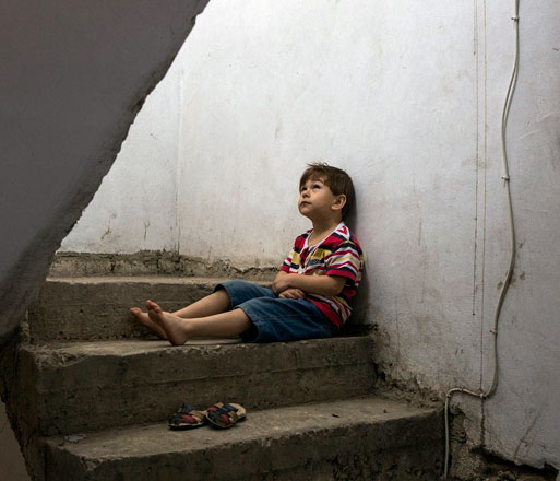 Omar sits for a portrait in the stairwell of the building where he and his family live as refugees in Lebanon (Photo courtesy of UNHCR)