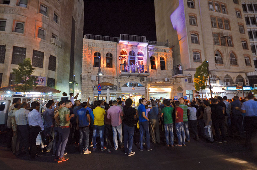 A crowd gather Wednesday night as musicians play from a balcony of an old building’s balcony in downtown Amman as part of an initiative to attract public attention to the city’s architectural heritage (Photo by Muath Freij )