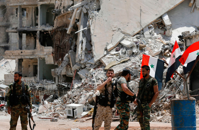 Pro-government forces attend a flag raising ceremony at the entrance of Al Hajar Al Aswad neighbourhood on the southern outskirts of the capital Damascus on Thursday, after the regime seized the Yarmouk Palestinian camp and adjacent neighbourhoods of Tadamun and Al Hajar Al Aswad earlier in the week from Daesh, putting Damascus fully under its control for the first time since 2012 (AFP photo)