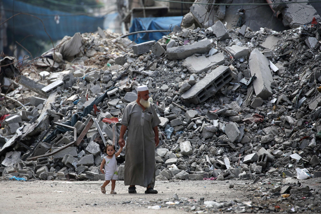 Elderly man holds a child by the hand as he walks past a building levelled by Israeli bombardment in the Bureij refugee camp in central Gaza Strip on August 25, 2024 (AFP photo)
