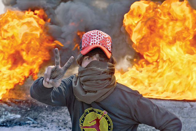 A masked anti-gov't protester flashes the victory gesture as he stands before flaming tyres at a make-shift roadblock in the central Iraqi holy shrine city of Najaf on Monday (AFP photo)