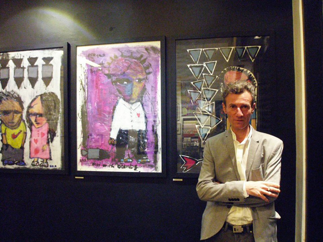 Rafik Majzoub poses in front of his paintings at Jacaranda Images gallery in Amman on Tuesday (Photo courtesy of Jacaranda Images)