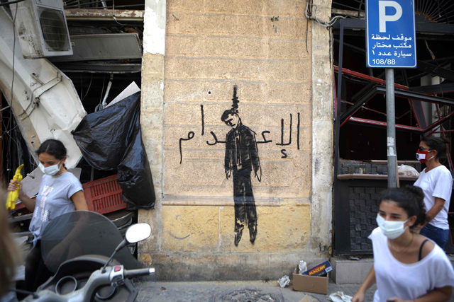 In this file photo taken on August 7, members of the Lebanese civil society carrying brooms used for clearing debris, walk past a wall painting depicting a hanged politician and reading (death sentence in Arabic) in the partially damaged Beirut neighbourhood of Mar Mikhael (AFP photo)