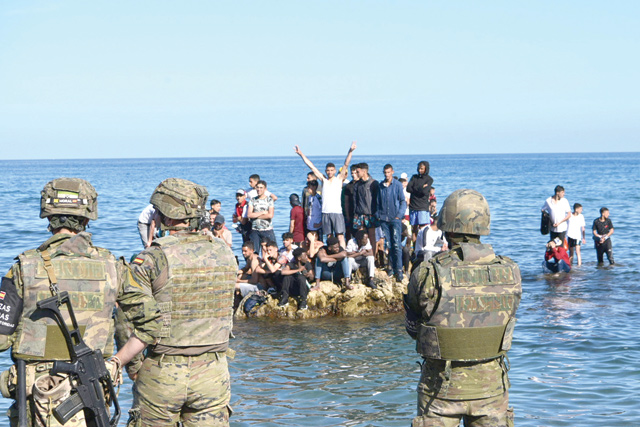 Spanish soldiers stand guard as migrants stand on rocks off the shore of the Spanish enclave of Ceuta, on Tuesday (AFP photo)