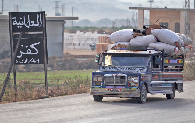 Displaced Syrians from a village in southern Idlib drive past a sign reading in Arabic: ‘Secularism is infidelity’ as they head on the Damascus-Aleppo motorway towards the northern part of the rebel-held province on Friday (AFP photo)