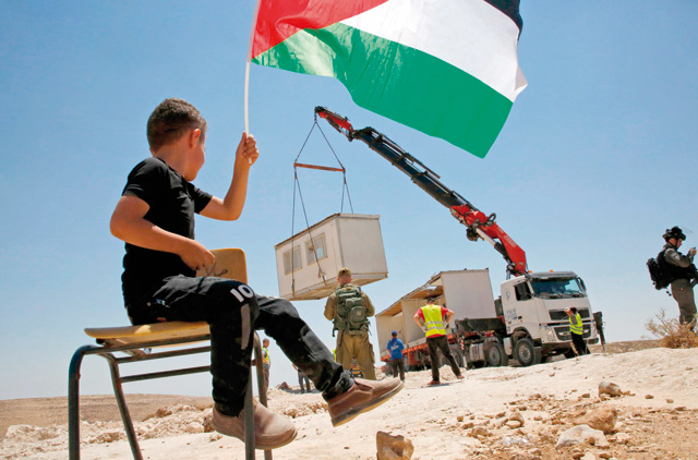 A Palestinian boy waves a national flag by Israeli forces evacuating protesters from a school site being demolished in the village of Yatta, south of the West Bank city of Hebron, on Wednesday (AFP photo)