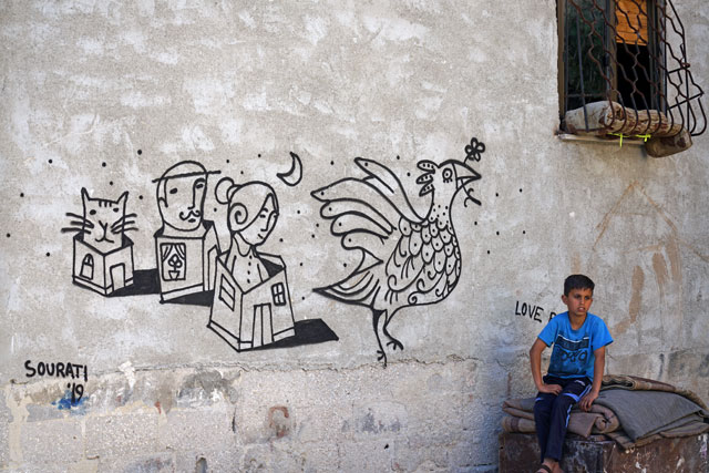 In this undated photo, a boy can be seen sitting in front of a mural painted by German artist Duo Sourati during the 2019 Baladk street art festival in Amman (Photo courtesy of Al Balad Theatre)