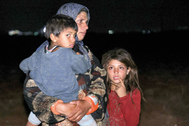 A woman stands carrying a boy next to another girl in the aftermath of Syrian government forces' bombardment, at a camp for those displaced by conflict in Sarmin in the rebel-held part of Syria's northwestern Idlib province late on Saturday (AFP photo)
