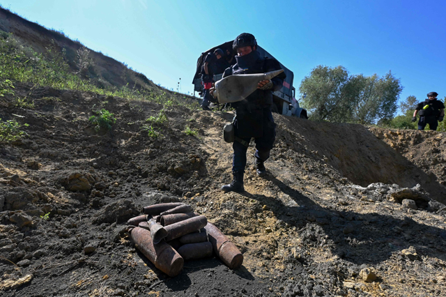 A member of the State Emergency Service of Ukraine collects unexploded ammunition from World War II and the current Russian invasion to detonate them, during a clearance patrol near the village of Zolochiv, Kharkiv Region, on Friday (AFP photo)