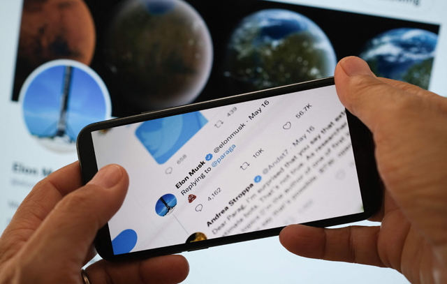 In this illustration photo taken on Monday, Elon Musk's reply Tweet to Parag Agrawal, the CEO of Twitter, showing a poop emoji is displayed on the screen of a smartphone with Musk Twitter page in the background in Los Angeles (AFP photo)