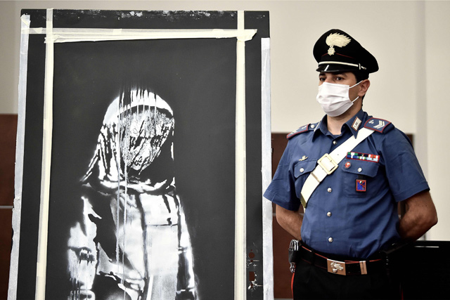  In this file photo taken on June 1, an Italian Carabinieri poses near a piece of art attributed to Banksy, that was stolen at the Bataclan in Paris in 2019, and found in Italy, during a press conference in L'Aquila (AFP Photo)