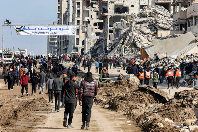 People gather by a banner welcoming people near the rubble of a collapsed building along Gaza's coastal al-Rashid Street for people to cross from the southern Gaza Strip into Gaza City on Sunday (AFP photo)