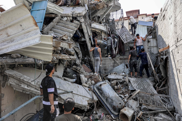 People gather outside a collapsed building as they attempt to extricate a man from underneath the rubble following Israeli bombardment in the Saftawi district in Jabalia in the northern Gaza Strip on Tuesday (AFP photo)