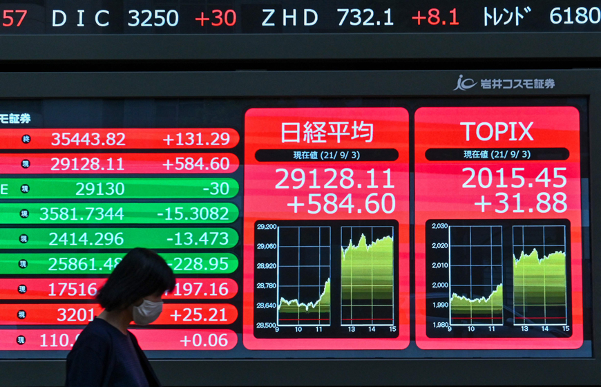 A woman walks past an electronic quotation board displaying the closing share prices of the Tokyo Stock Exchange (centre) in Tokyo, on Friday (AFP photo)