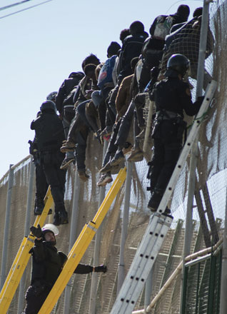African migrants sit on top of a border fence during an attempt to cross into Spanish territories, between Morocco and Spain’s North African enclave of Melilla, Saturday (Reuters photo)