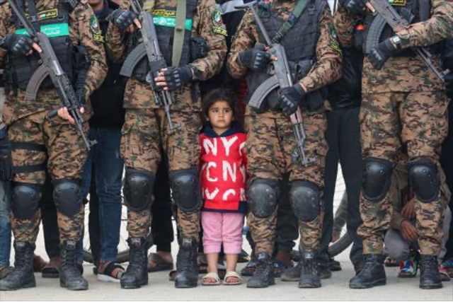 A Palestinian girl stands between Hamas fighters as she watches the handover of three Israeli hostages to a Red Cross team in Deir El Balah, central Gaza, on February 8, 2025 (AFP photo)