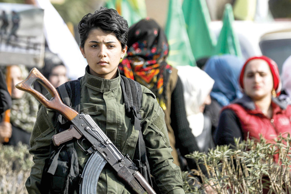 A Syrian Kurdish woman fighter holds a Kalashnikov assault rifle as she stands while others march past during a demonstration in the northeastern Syrian city of Qamishli on Sunday, as they mark the International Day for the Elimination of Violence against Women (AFP photo)