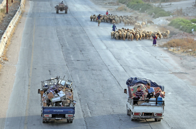 Syrian families from the southeastern Idlib province and the northern countryside of Hama fleeing battles with trucks loaded with their belongings, drive past a flock of sheep on the highway, near Maaret Al Numan in the southern Idlib province, on Wednesday (AFP photo)