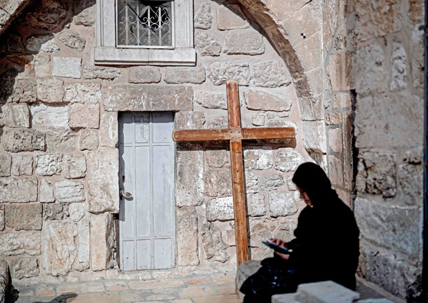 A woman sits near a wooden cross outside the Church of the Holy Sepulchre in the Old Jerusalem on Wednesday (AFP photo)