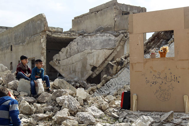 Children watch a puppet show performed by a Syrian actor, through a makeshift puppet theatre set up among the rubble of collapsed buildings in the town of Saraqib in the rebel-held northern Idlib province, on Wednesday (AFP photo)