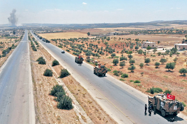 A convoy of Turkish military vehicles is photographed near the town of Maar Hattat as smoke billows in the background, during reported air strikes in northern Syria's Idlib province, on Monday (AFP photo)