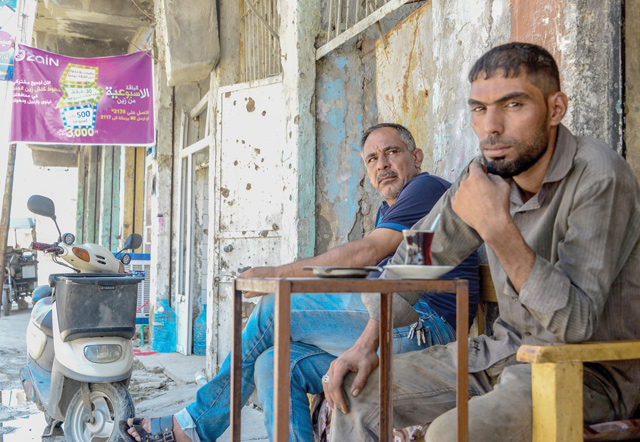 Men sit in front of shops in the old city of Mosul in northern Iraq on Monday  (AFP photo)