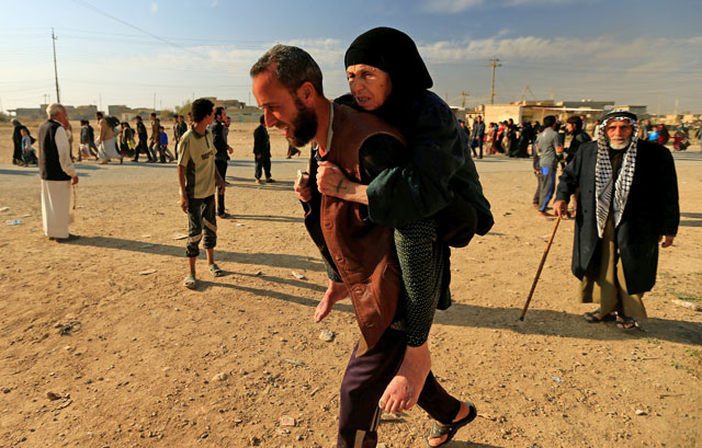 A displaced man, who had fled from Hammam Al Alil, south of Mosul, Iraq, to head to safer territory, carries his mother on Sunday (Reuters photo)