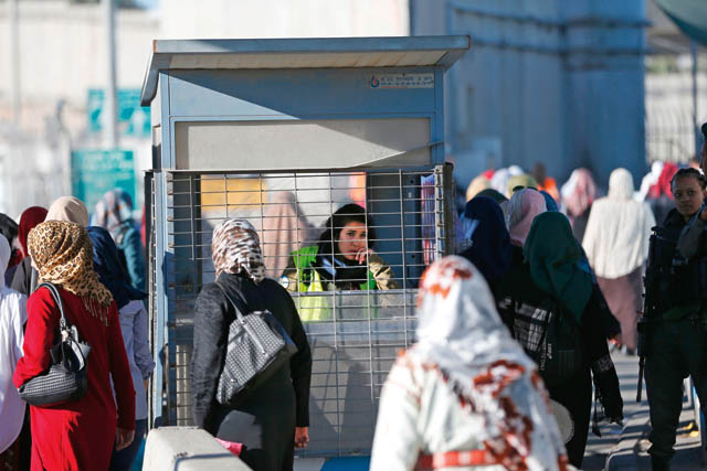 Palestinians walk past an Israeli forces member as they make their way through the Israeli Qalandia checkpoint, in the occupied West Bank between Ramallah and Jerusalem, to attend Friday prayer of the holy fasting month of Ramadan in Jerusalem’s Al Aqsa Mosque, on Friday (AFP photo)