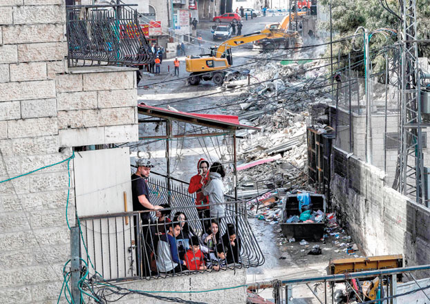 A Palestinian family watch from a balcony as excavators of the Jerusalem municipality demolish over a dozen shops in the Arab-inhabited Shuafat refugee camp in Israeli-annexed East Jerusalem on Wednesday, which authorities said were built without a permit (AFP photo)
