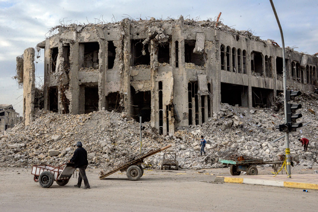 An Iraqi pushes his cart past the rubble of the destroyed seven-storey Chadirji building, designed by celebrated Iraqi architect Rifat Chadirji in the 1960s, on Sunday, in the city of Mosul (AFP photo)