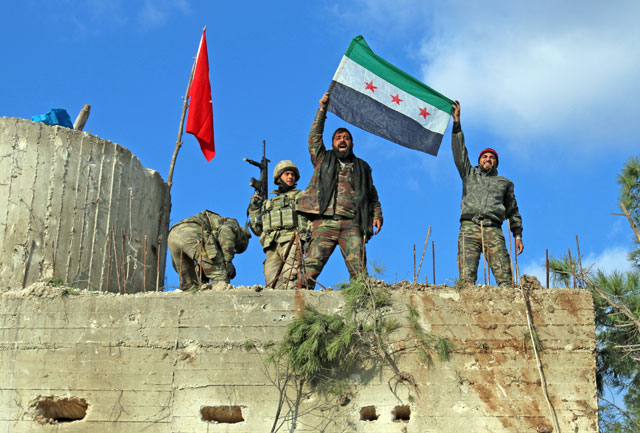 Turkish-backed Syrian rebels, wearing red ribbons, raise a rebel flag as they stand alongside Turkish soldiers on a mountain on the Syrian-Turkish border, north of Azaz, on Sunday (AFP photo)