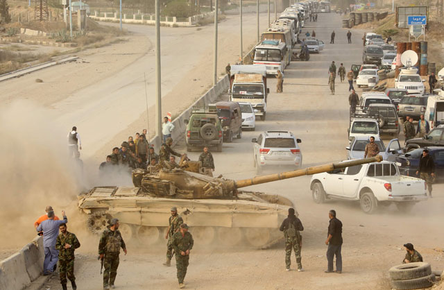 Syrian regime forces gather near buses waiting at the entrance of Harasta in Eastern Ghouta, on the outskirts of Damascus, on Thursday, after a deal was struck with the rebels in the area to evacuate the town (AFP photo)